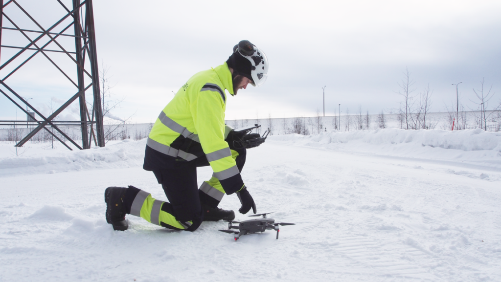 Kuvassa mies polvillaan talvisessa maisemassa työhaalarit päällä. asentaa dronea. Blogi: Virve 2 vaivattomasti käyttöön - Rejlers